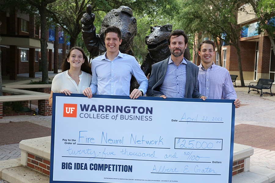 A group of four young entrepreneurs smiling and holding a large $25,000 check in front of the bronze alligator statues on the University of Florida campus. The check is from the Entrepreneurship & Innovation Center’s Big Idea Competition.