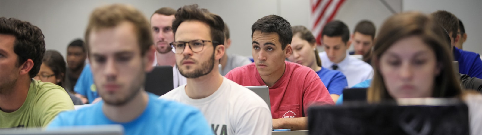 A classroom filled with attentive accounting students, focused on their laptops and notebooks during a lecture.