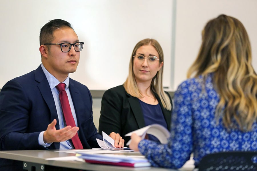 Two business students attentively listening and discussing with a presenter during a case competition presentation.