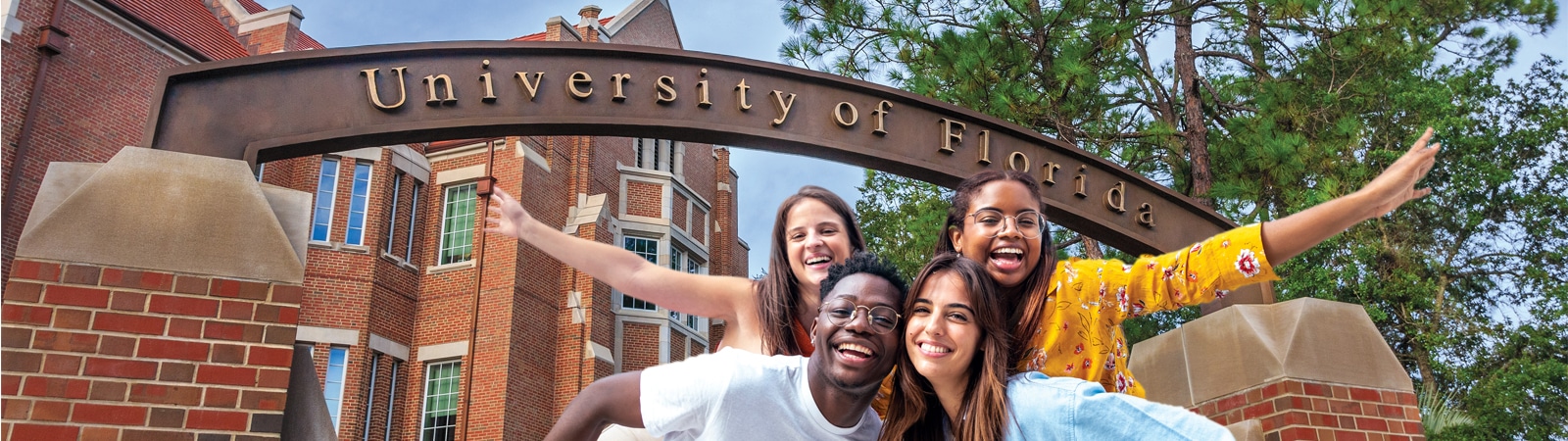 A diverse group of four University of Florida students pose happily under the iconic University of Florida archway on campus.