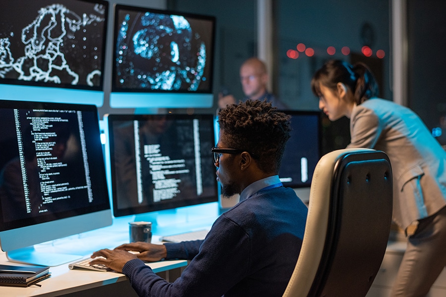 Young it-engineer decoding data while sitting in front of computer monitors.