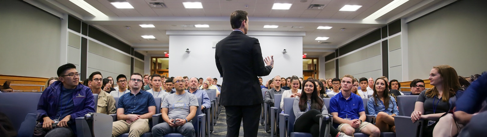 A speaker addresses a large, attentive audience of students and professionals seated in an auditorium during the Heavener International Case Competition.