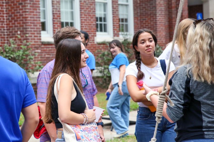 A group of college students standing outdoors on campus, engaged in conversation and socializing in a relaxed atmosphere.