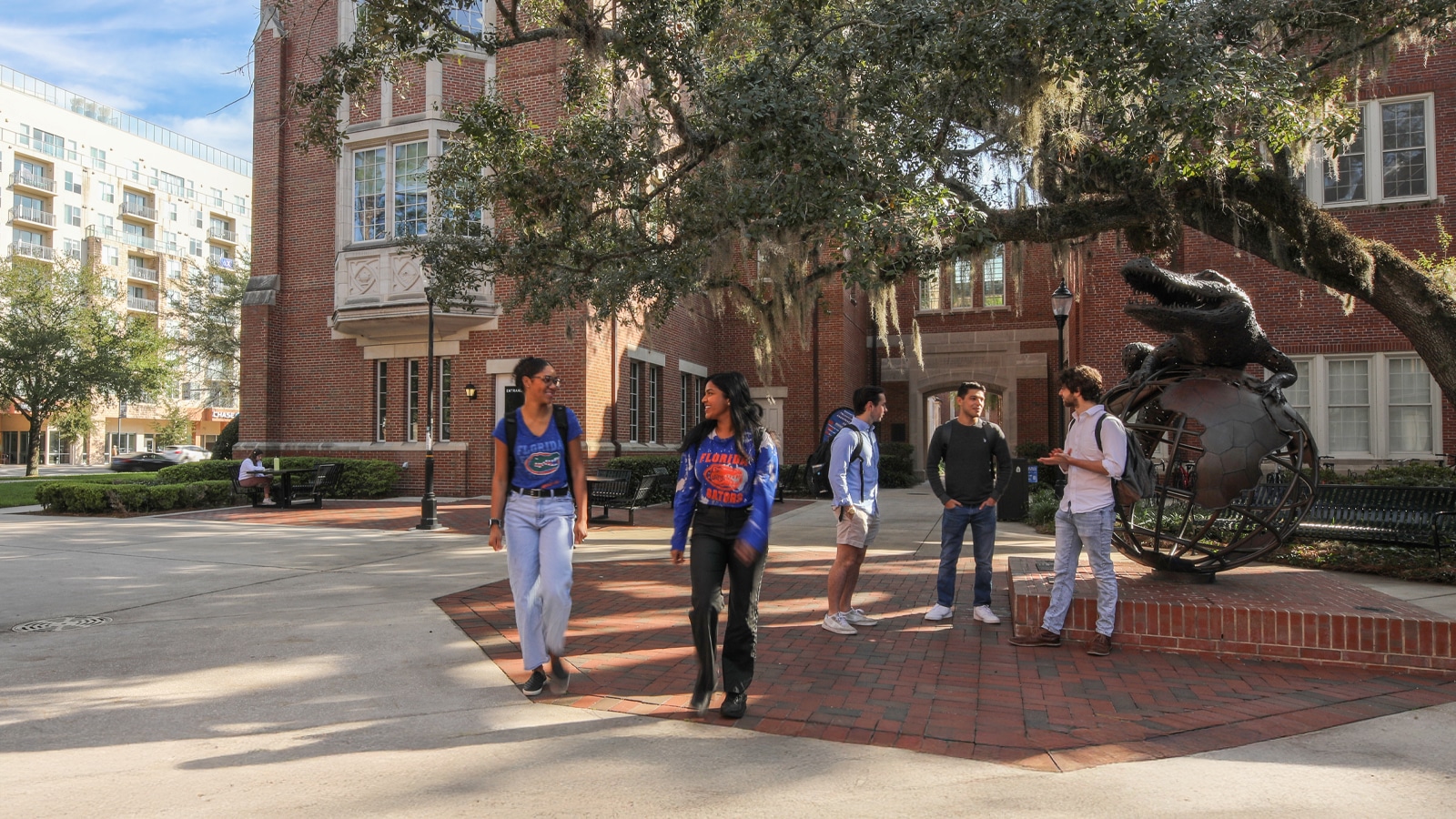 Students gather and talk in front of Heavener Hall, with the iconic Gator statue on display under a sprawling oak tree at the University of Florida’s Warrington College of Business.