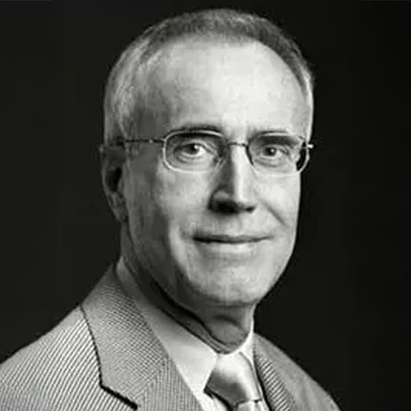 Black and white headshot of Kenneth McGurn, an older man with short gray hair and glasses, wearing a light-colored jacket and a tie, looking directly at the camera with a neutral expression.