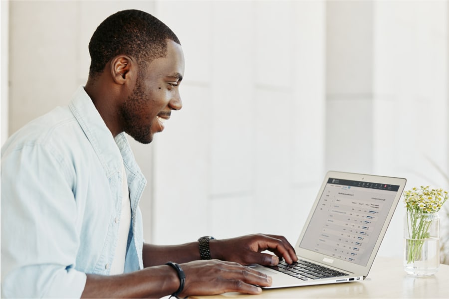 A smiling student works on a laptop at a bright desk, viewing an online course dashboard with several modules in progress.