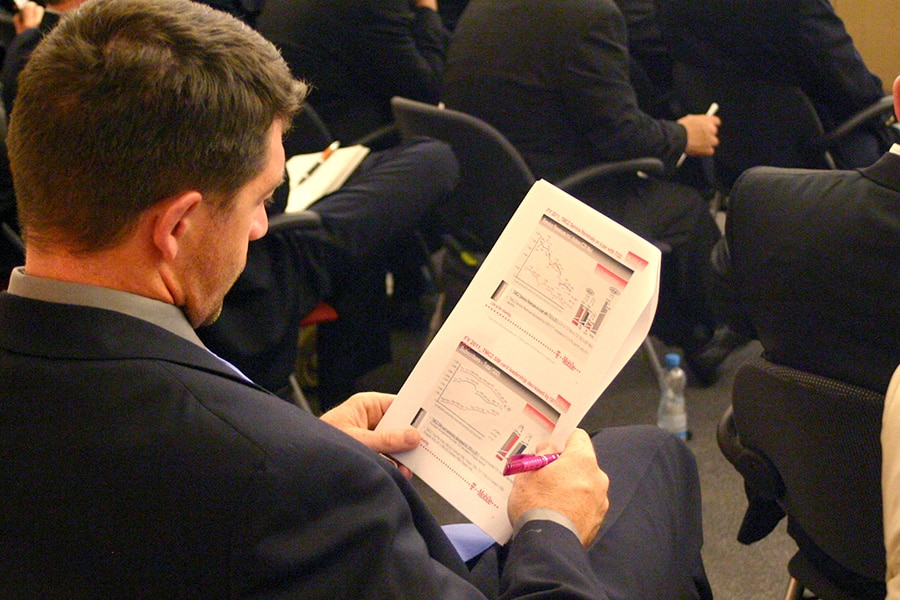 Man in professional attire sitting and looking through a printed report with many graphs and data.