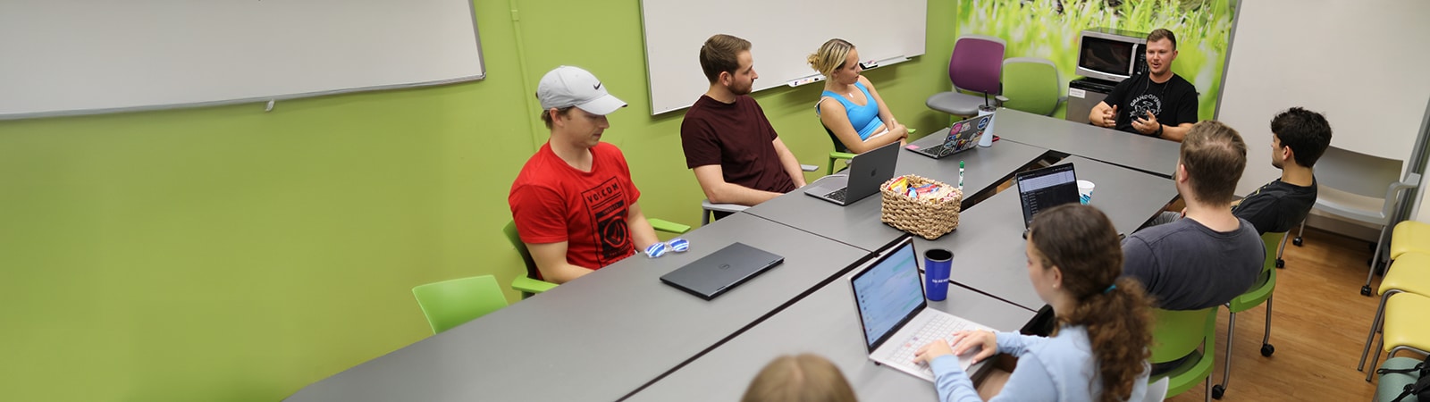 A man speaking to a group of students around a table. 
