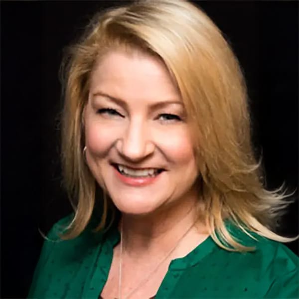 Headshot of Mary Pat Dunleavy, a smiling woman with blonde hair wearing a green top, posed against a black background.