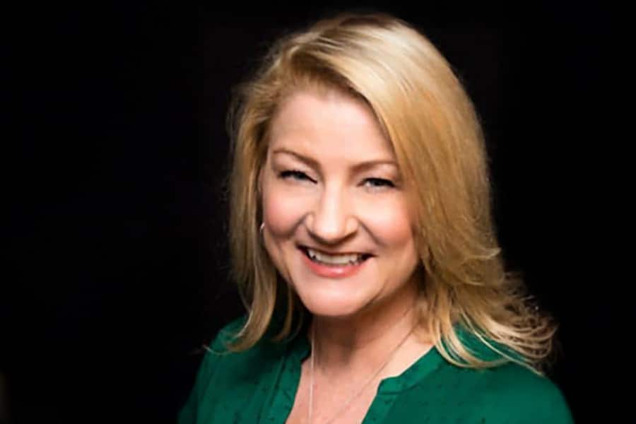 Headshot of Mary Pat Dunleavy, a smiling woman with blonde hair wearing a green blouse, against a black background.