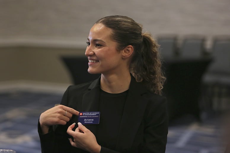 Young woman in professional attire pointing to her student nametag.