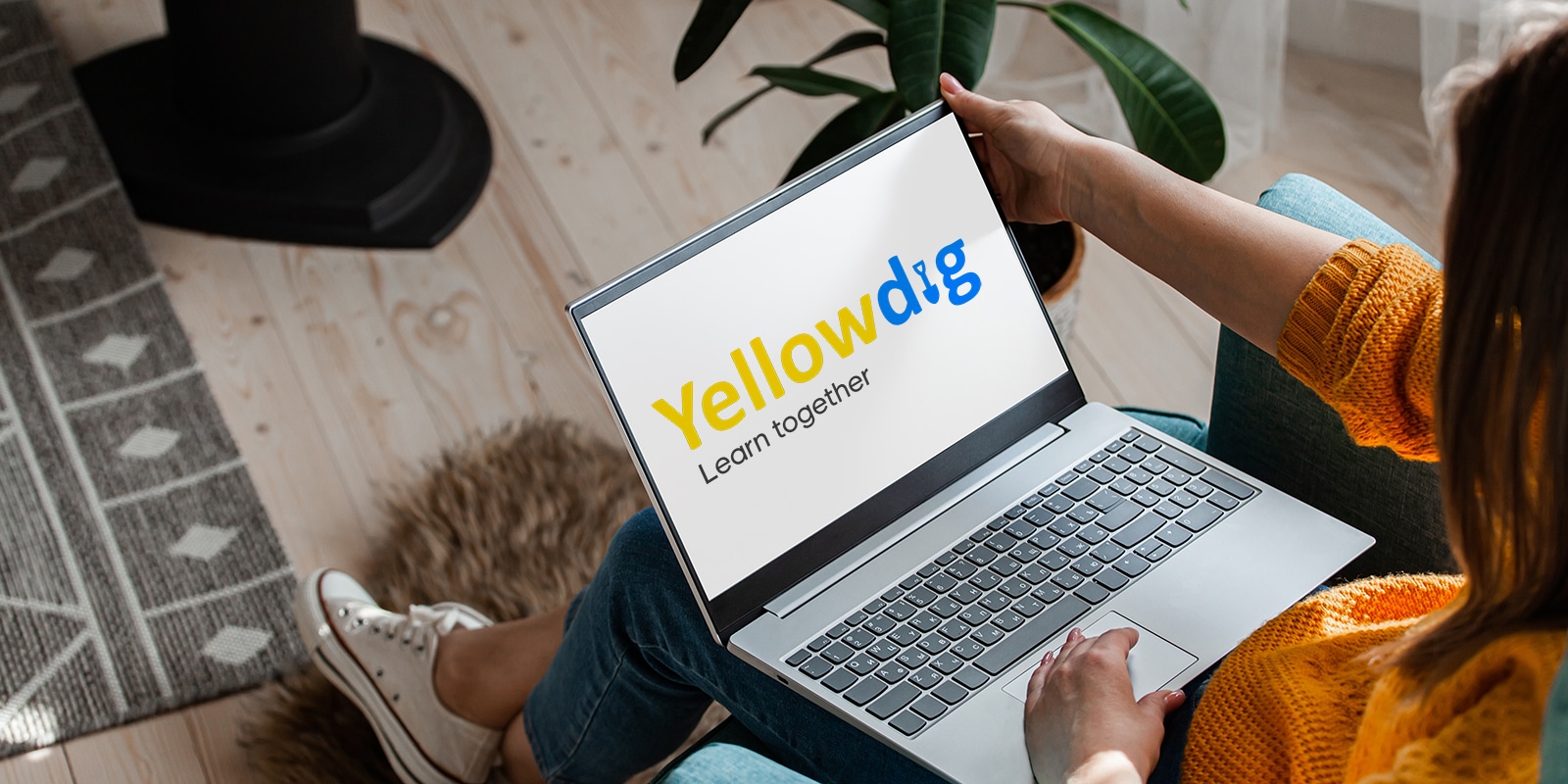 A laptop open on the user's lap shows the logo for Yellowdig, a communication platform used by UF Warrington Online BABA students