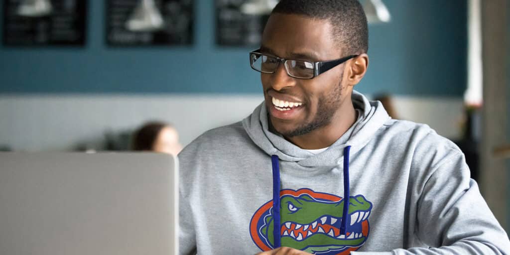 A student from UF Warrington's Online BSBA program wearing a Gator hooded sweatshirt uses a laptop while sitting down