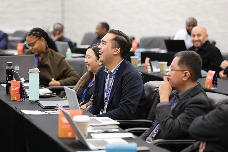 A group of professionals sitting at conference tables with their laptops and notepads.