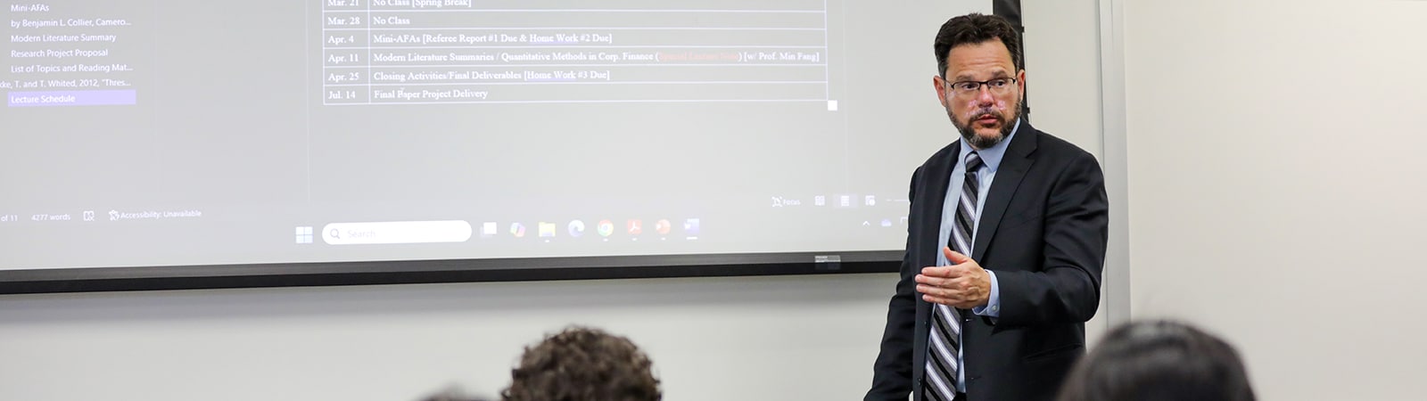 A professor discusses a research method, pointing to data on a screen, to a classroom of students enrolled in UF Warrington's PhD in Information Systems and Operations Management program