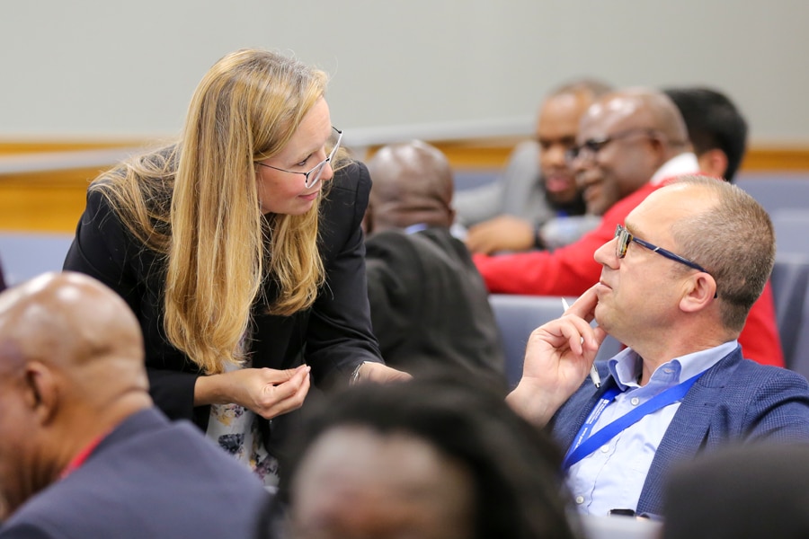 Araceli Castaneda, Director of Leadership Studies, speaks with a seated conference attendee at a PURC event, with other participants visible in the background.