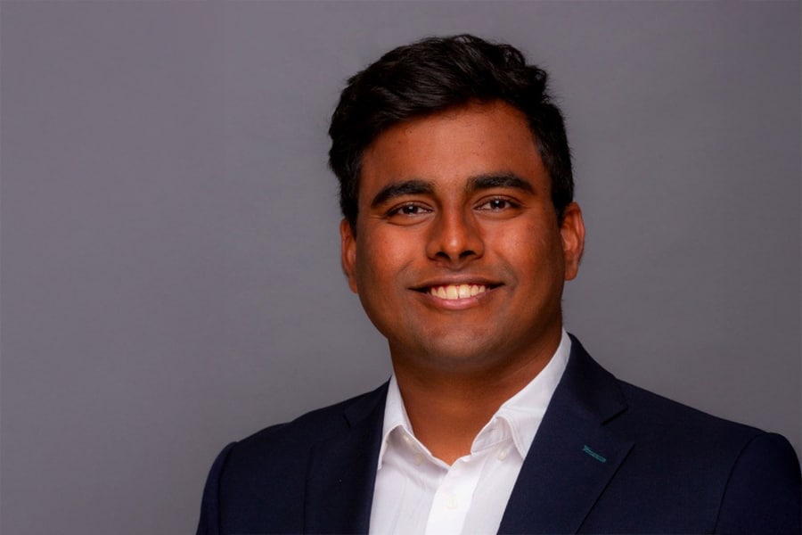 Portrait of Rajesh P. Shubhangam, a young man with dark hair, wearing a dark blazer and white shirt, smiling confidently against a plain gray background.