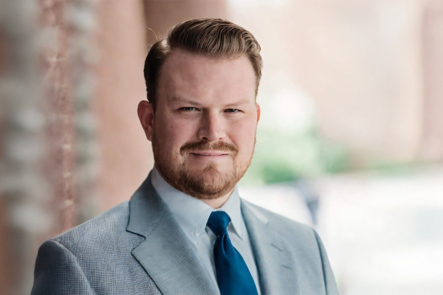 Professional headshot of Richard A. Duemmling wearing a light gray suit jacket, white shirt, and blue tie, smiling confidently outdoors.
