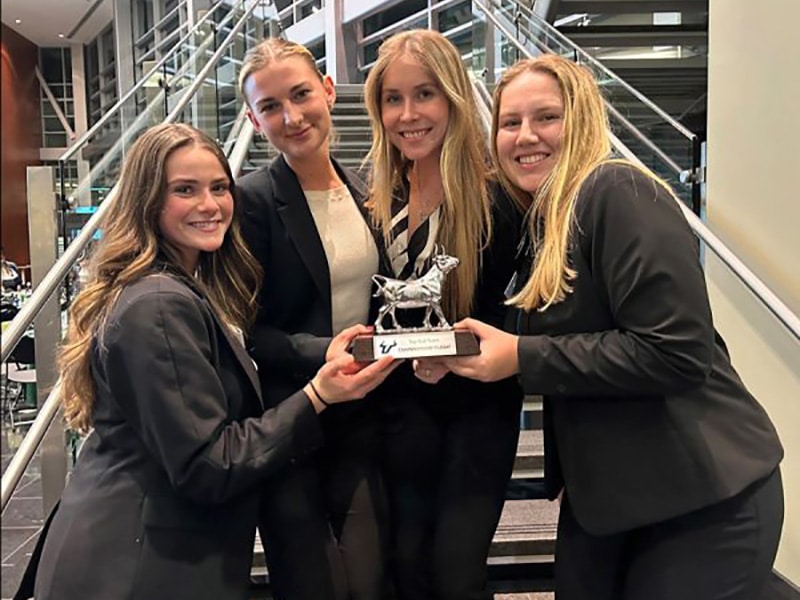 Four young women in professional attire holding a competition trophy.