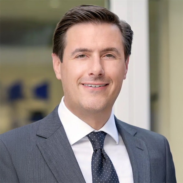 Headshot of Steven DeRose, a smiling man with dark hair, wearing a gray suit jacket, white shirt, and black polka-dot tie, posed against a soft-focus background.