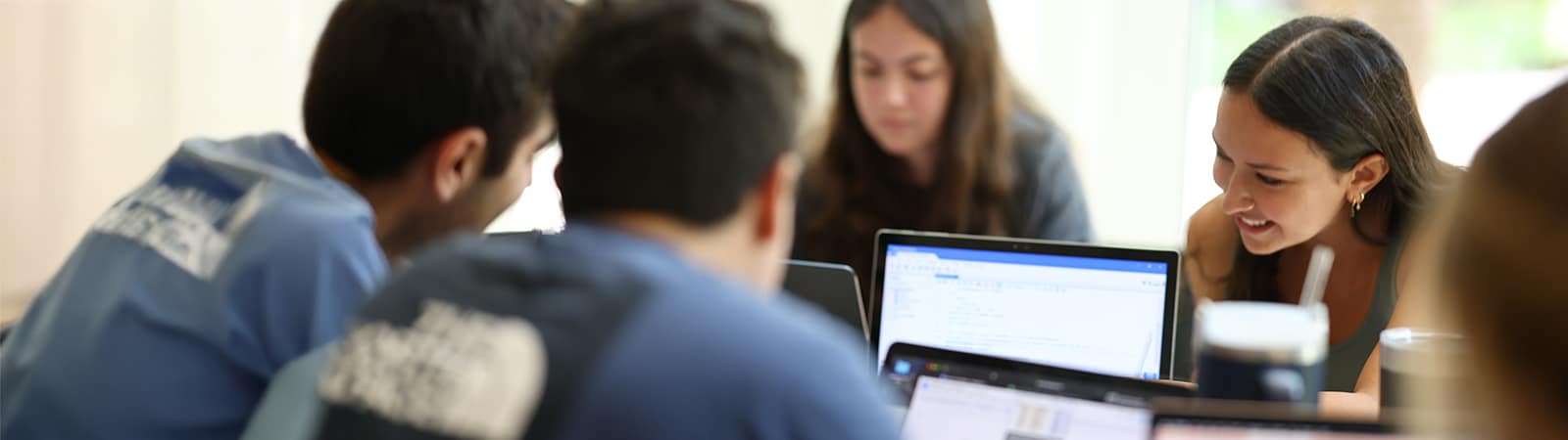 Students gathered around a table using laptops and email. 