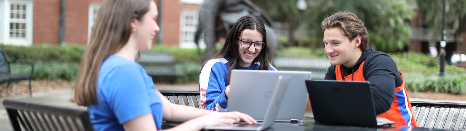 Group of students in Florida Gator shirts work at their laptops at a table outside.