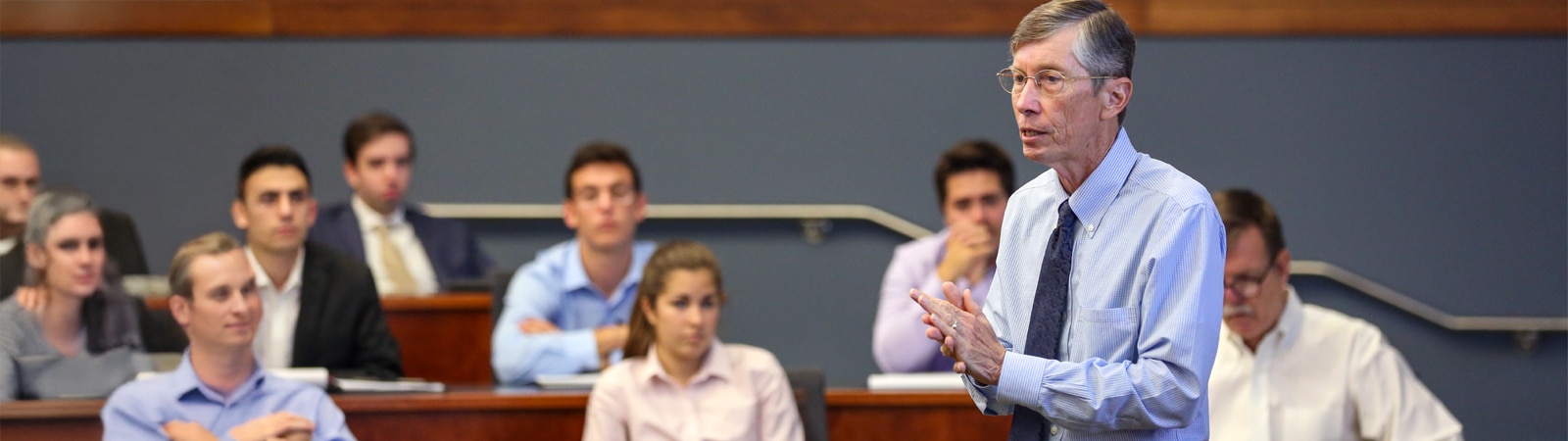 Professor Jay Ritter in a blue shirt and tie speaks thoughtfully to a classroom filled with attentive business students in a tiered lecture hall.