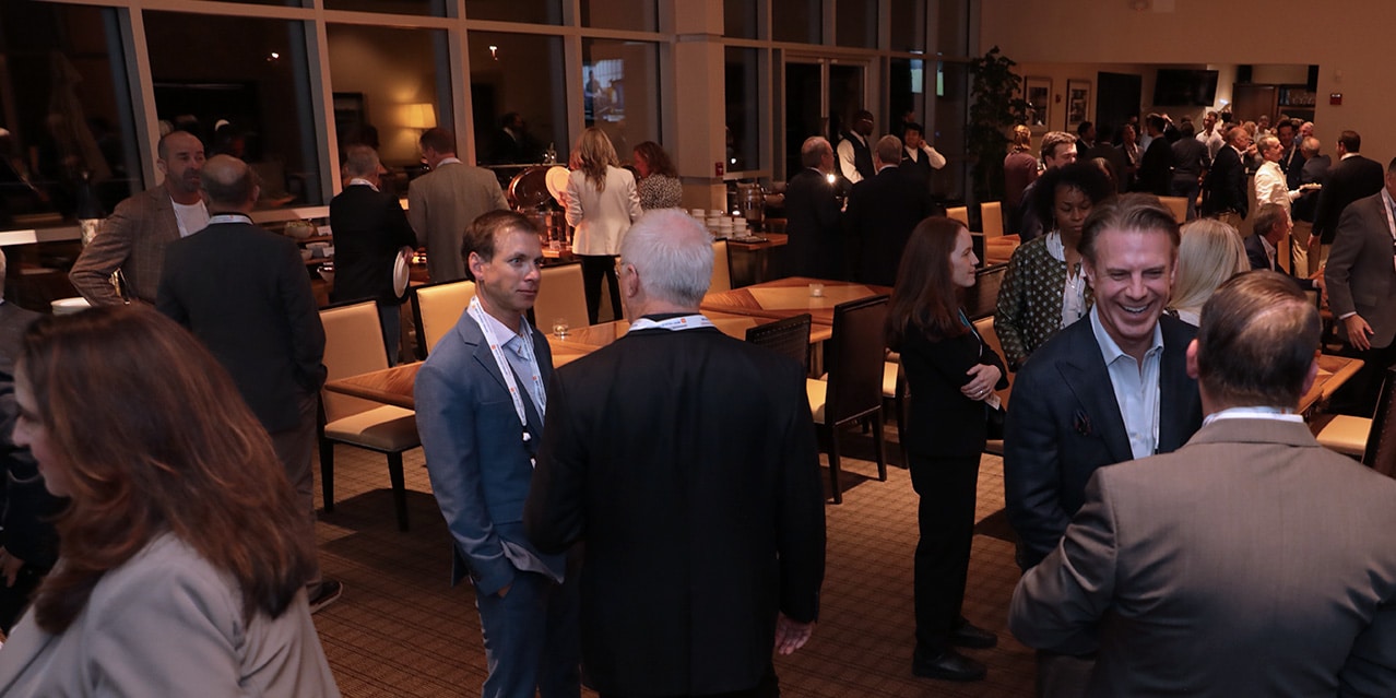 Business men and women in professional attire socializing in a large room.