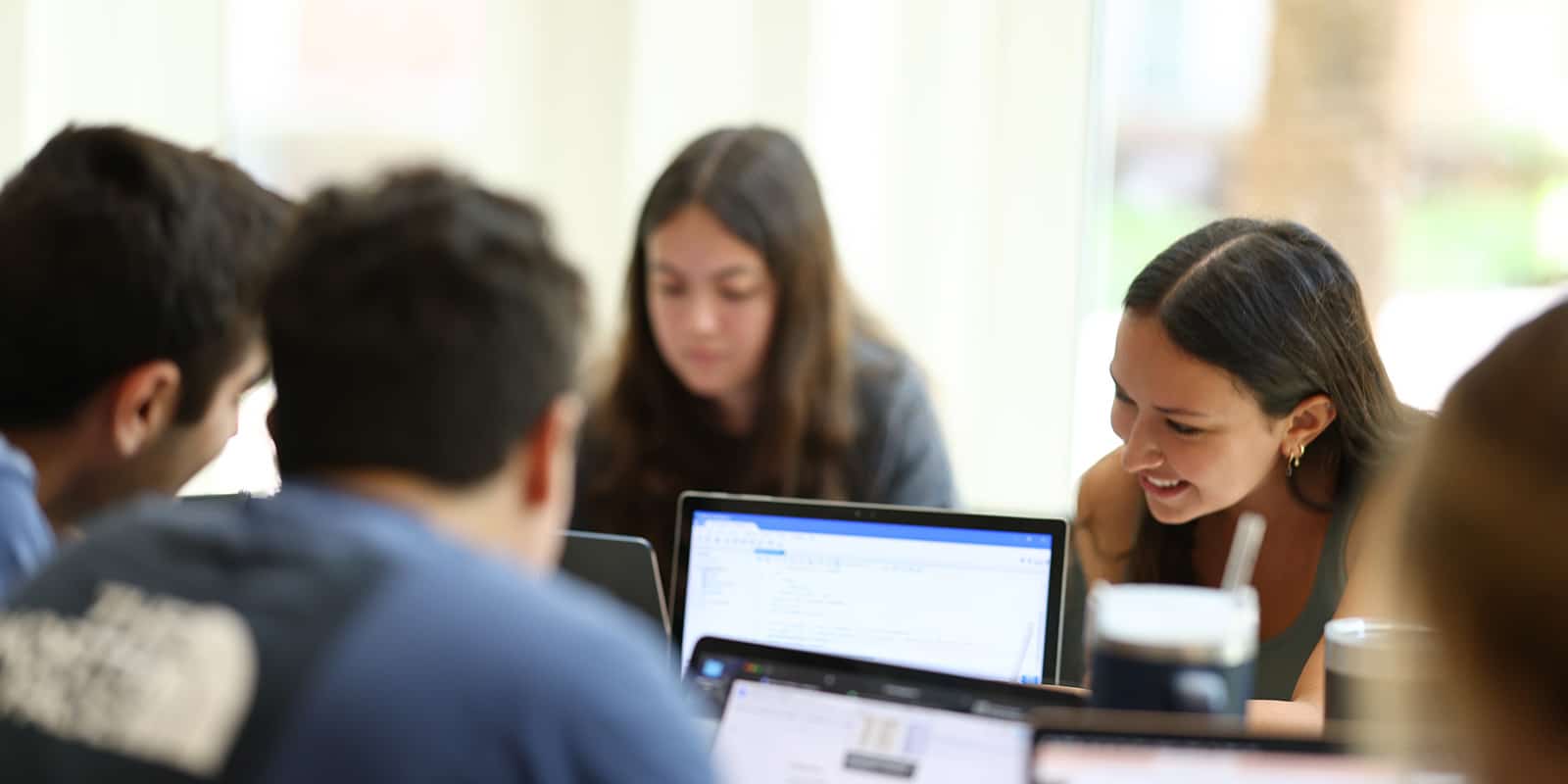 Undergrad students working on their laptops at a table together.