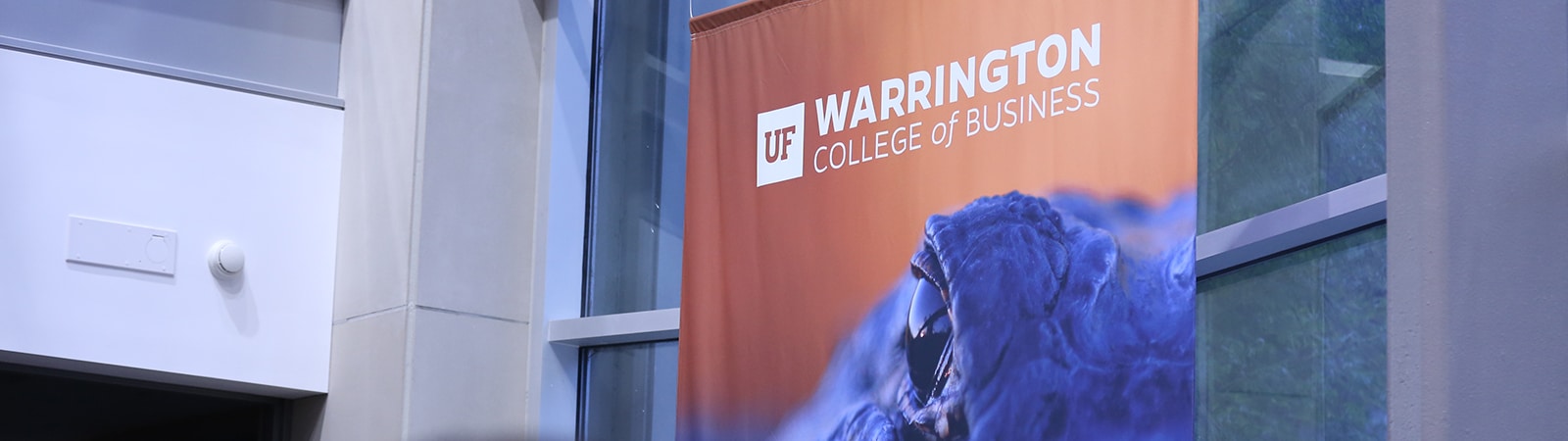 Warrington College of Business logo on a banner with a gator emerging from water.
