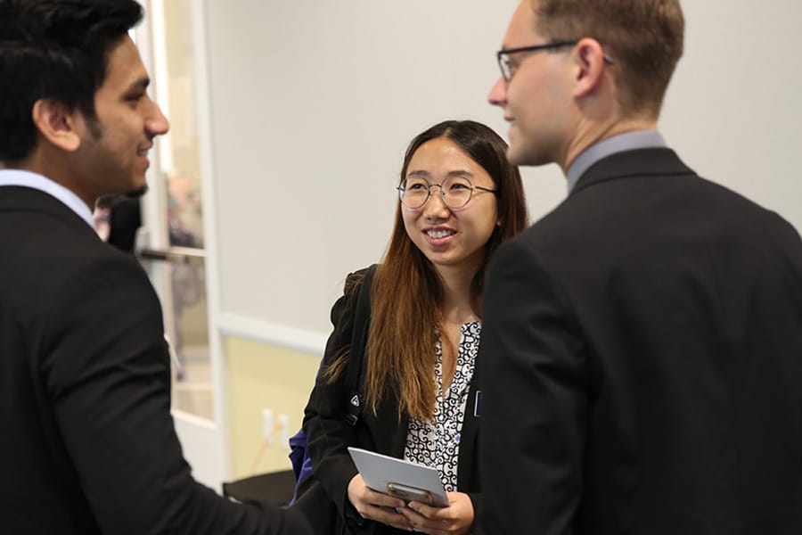 Three business students in professional attire socializing at a networking event.