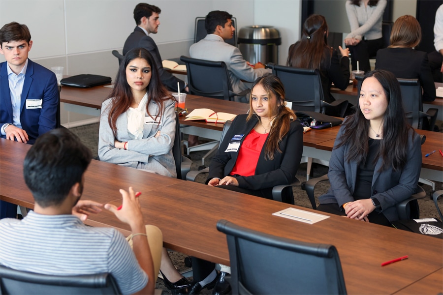 A diverse group of business students attentively listens to a male instructor seated at a conference table during an advanced portfolio risk management training session.