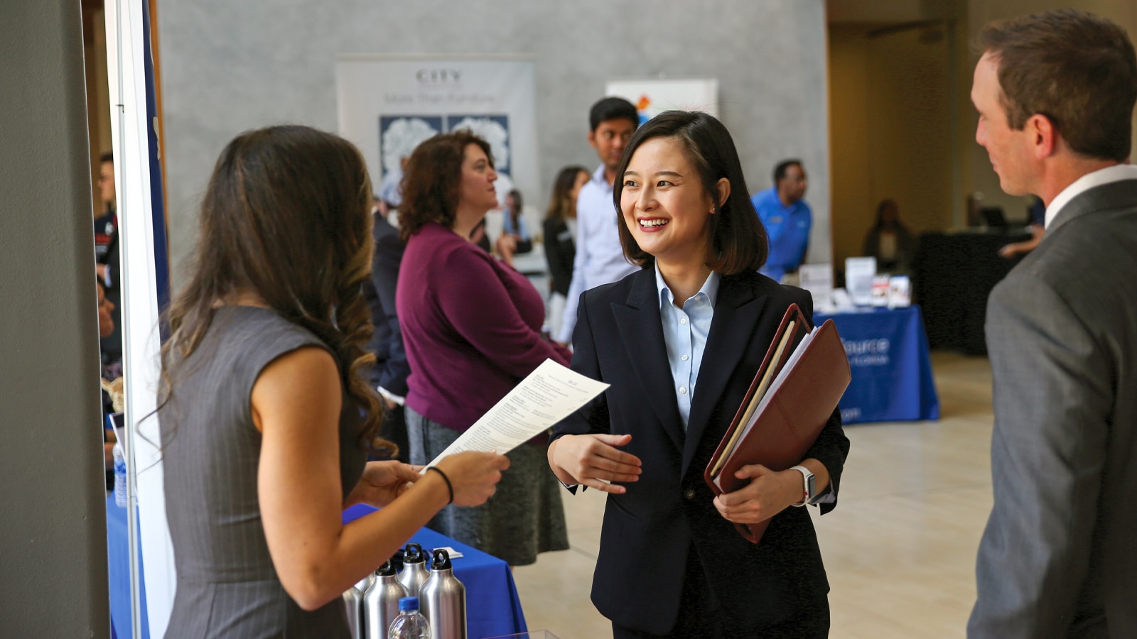 A student smiles while speaking with a recruiter at a business career fair.