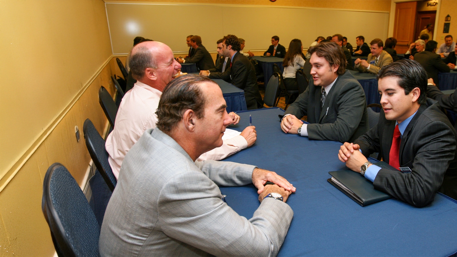 Students in business attire speak with professionals across tables during a career networking event.