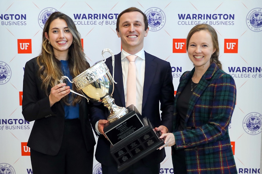 Three UF business students proudly hold a trophy in front of a Warrington College of Business backdrop