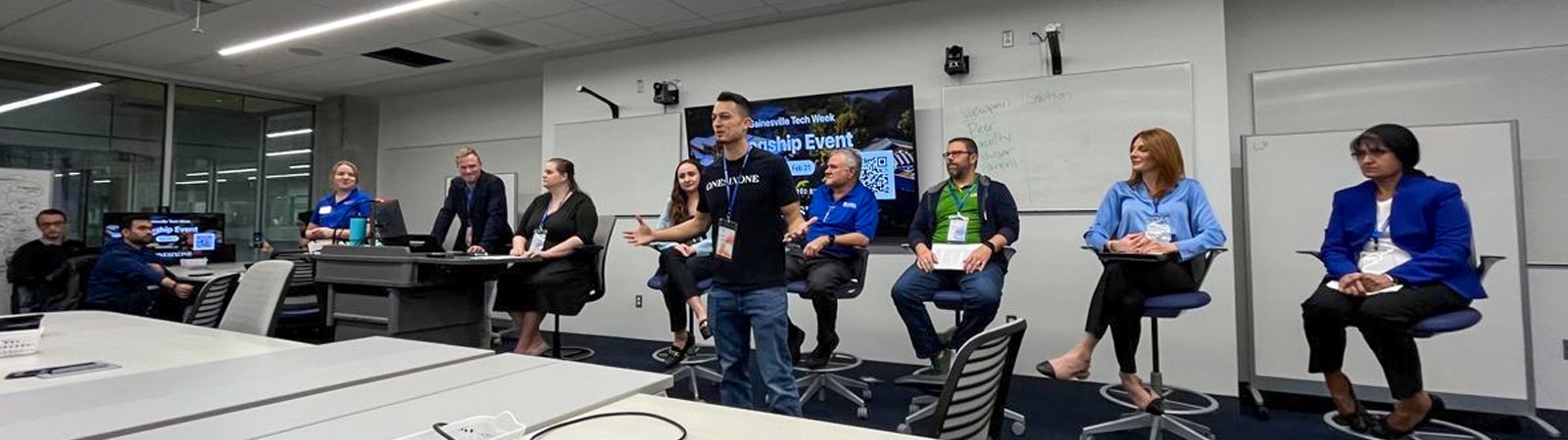 Student speaking to a room with a panel of speakers behind him. 
