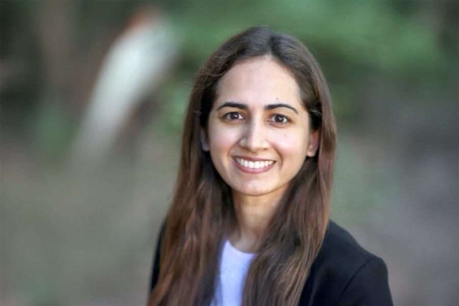 Portrait of Lucia Capuano, a young woman with long dark hair, smiling warmly at the camera. She wears a black blazer and a light top, standing outdoors with a blurred natural background.
