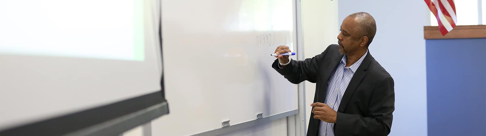 Professor writing on a white board in a classroom.