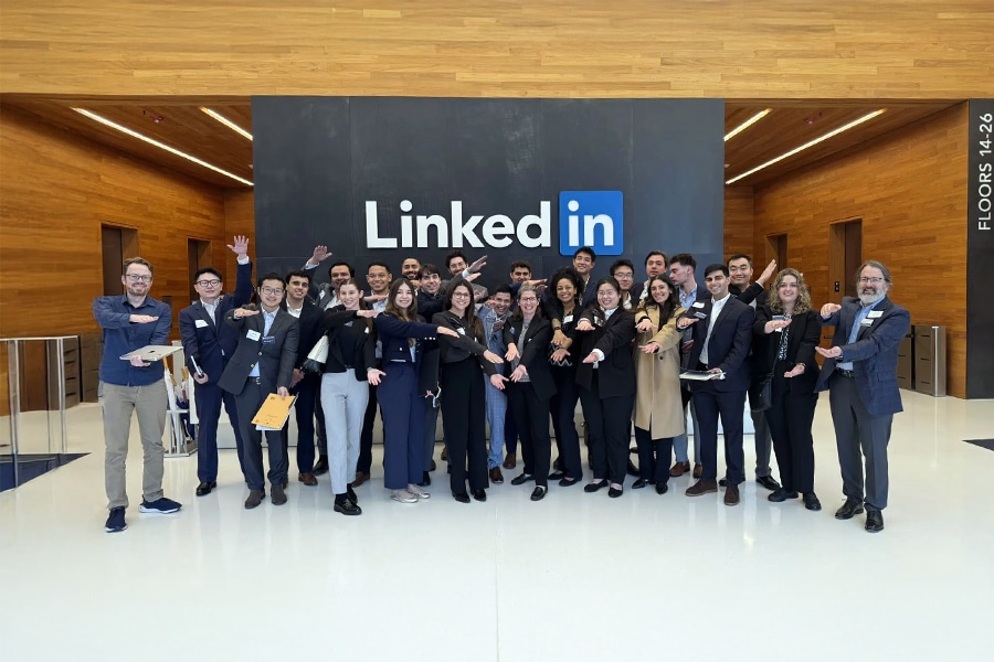 A group of students and faculty from the University of Florida Warrington College of Business pose enthusiastically inside the LinkedIn headquarters in Austin, Texas. They stand in front of a large LinkedIn logo on a black wall, extending their arms forward in a unified gesture. The lobby features wooden walls and white flooring.