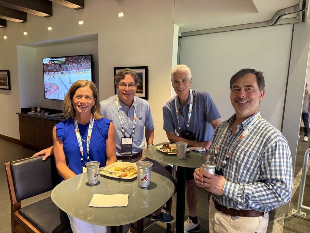 Four people pose for a photo while watching a baseball game. 