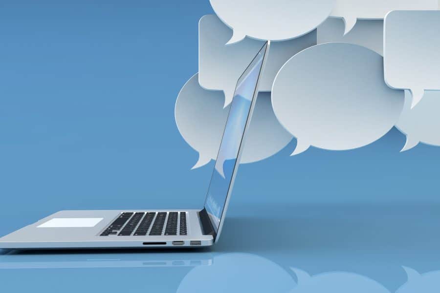 Communication technology, social networking, internet and online messaging concept, white empty speech bubbles and modern laptop computer on blue background with reflection