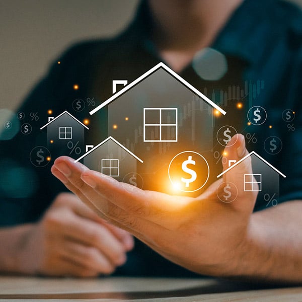 Close up of a man's hand on a table holding digital images of houses, dollar signs, percent symbols and a line graph.