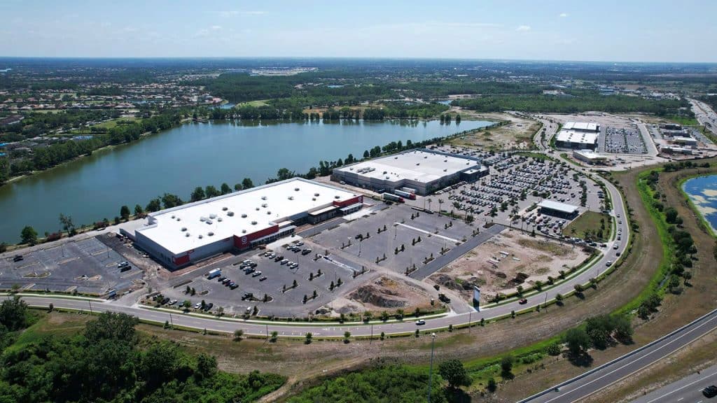 Aerial view of the Marketplace at Heritage Harbour in Bradenton, Florida shows large store buildings with a triangular lake in the background.