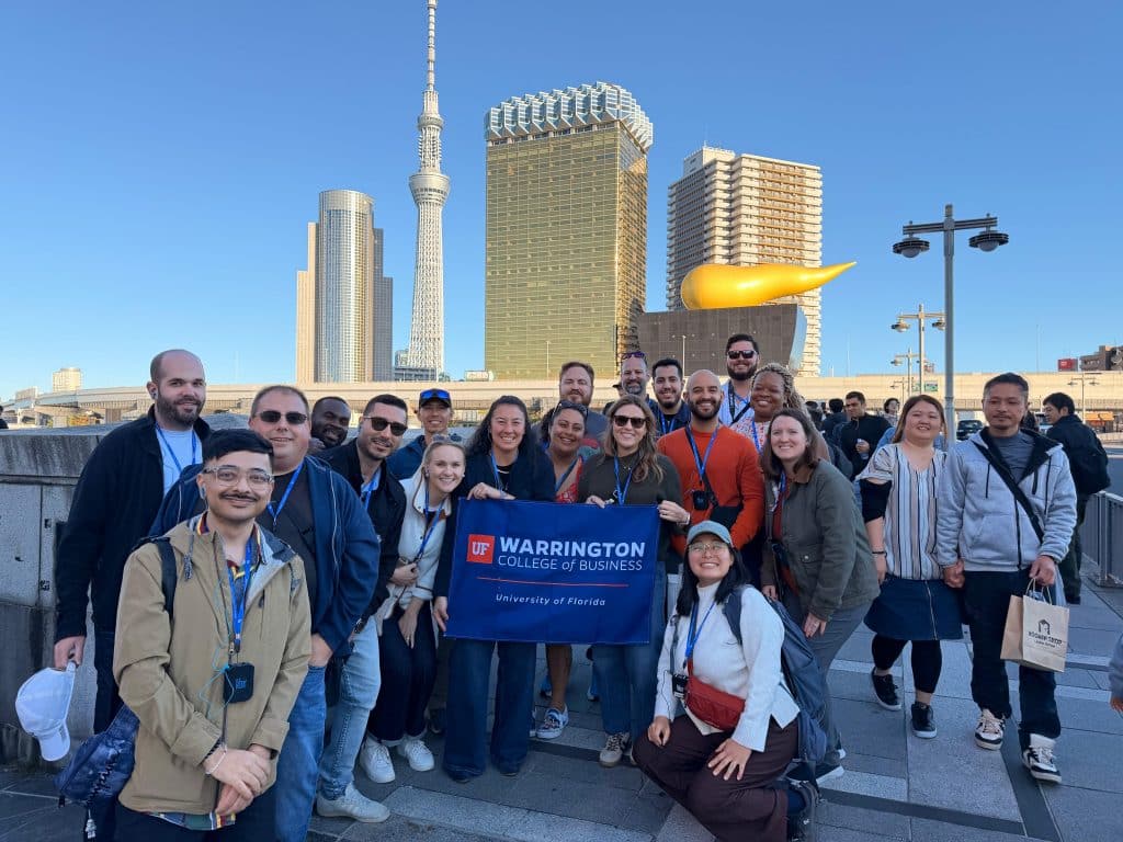 MBA student team in Japan holding a Warrington banner in front of tall city buildings