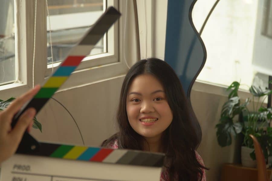 Juniper Nguyen smiles behind a movie clap board.