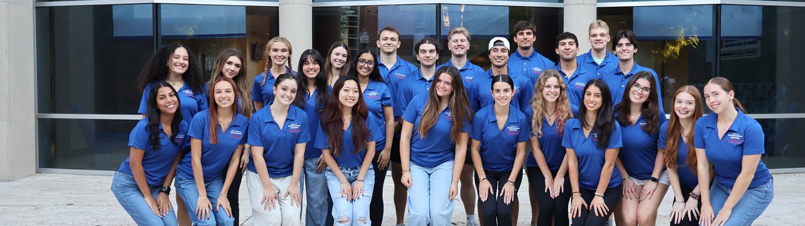 Graduate ambassadors, in their matching shirts, pose for a group photo with Hough Hall in the background