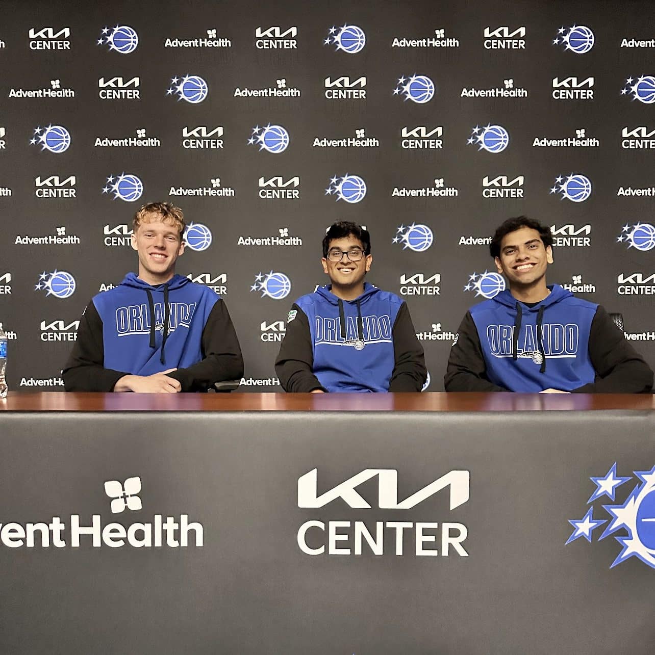 Tyler Rasmussen, Ahan Soni and Archit Namboodiri sitting at KIA Center, Advent Health and Orlando Magic Table