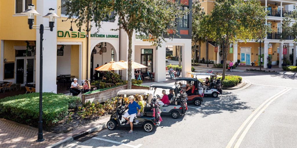 People parking their golf carts along the street in front of business with outdoor seating in Ave Marie
