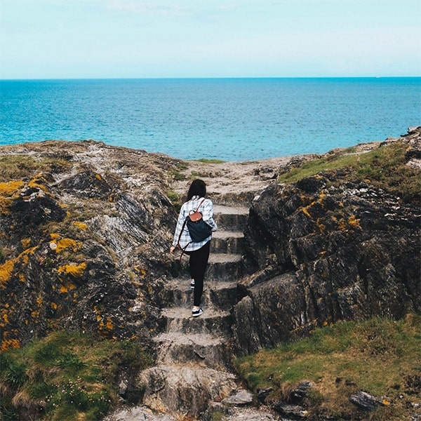 A woman climbs steps cut into the natural rock at Wicklow Coast, Ireland with the ocean in the background