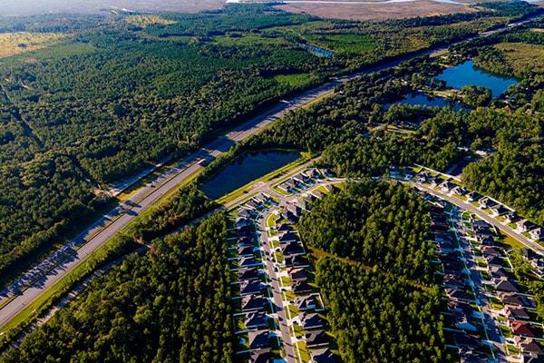 An aerial photo of homes next to an interstate going by small lakes and many acres of trees